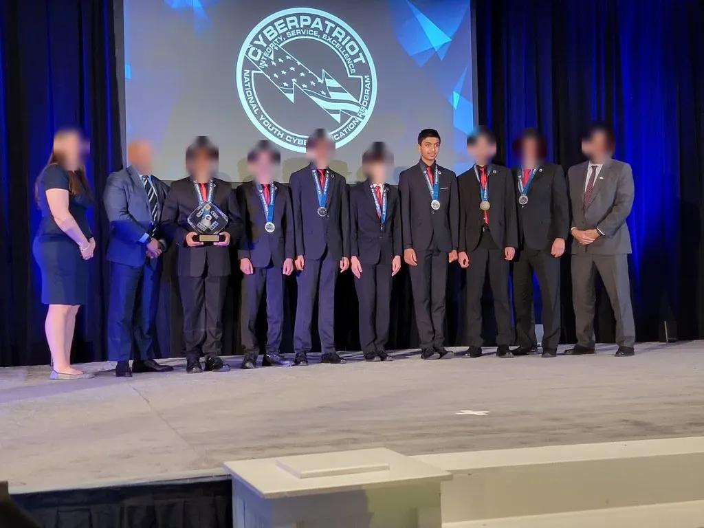 Aditya with CyberAegis on stage at the CyberPatriot National Finals; teammates' and officials' faces blurred