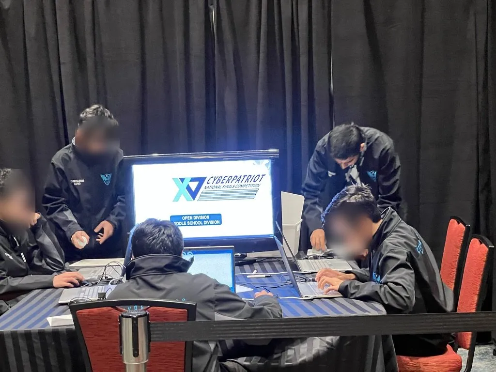 CyberAegis working at the CyberPatriot National Finals table; teammates' faces blurred