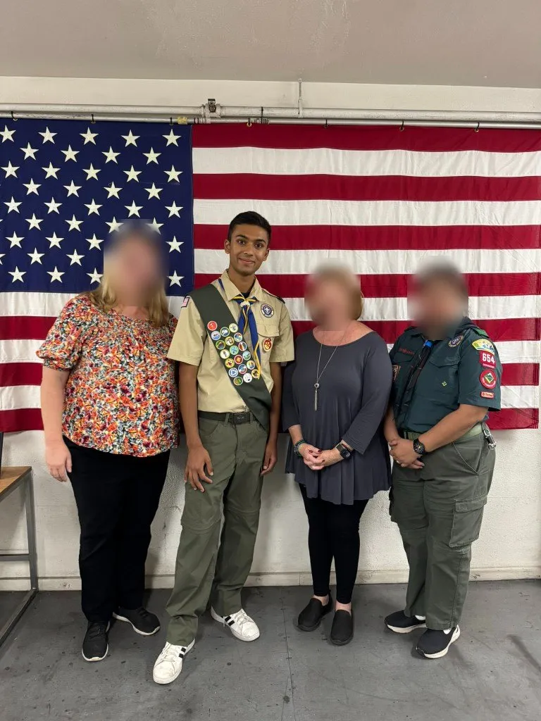 Aditya with three adult leaders in front of the flag; other faces blurred