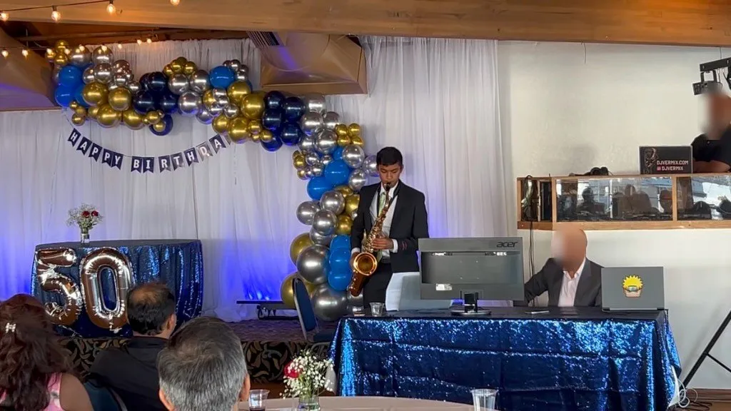 Aditya standing with his tenor saxophone at a birthday performance; other faces blurred