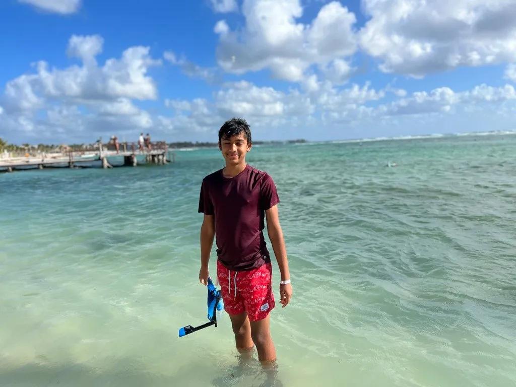 Aditya standing in clear turquoise water holding snorkel gear