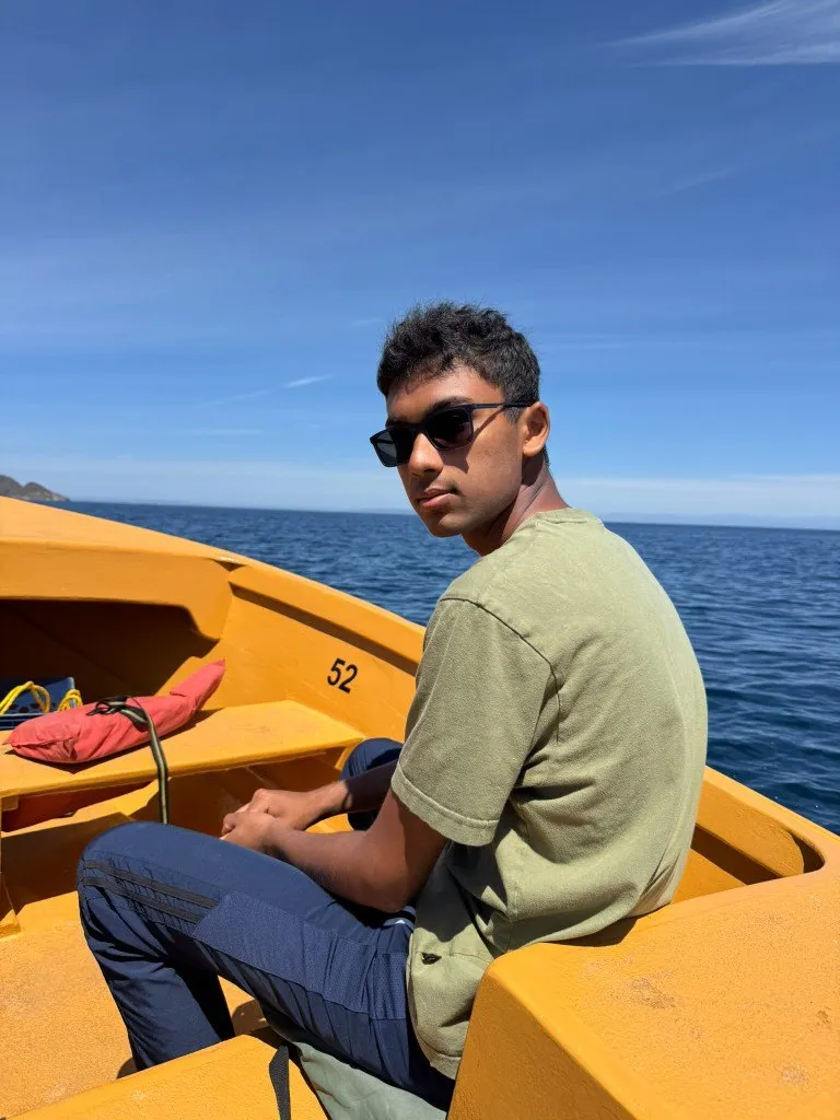 Aditya in sunglasses at the bow of a yellow boat on open ocean