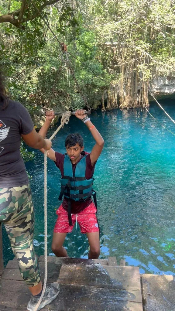 Aditya holding a rope swing above a turquoise cenote