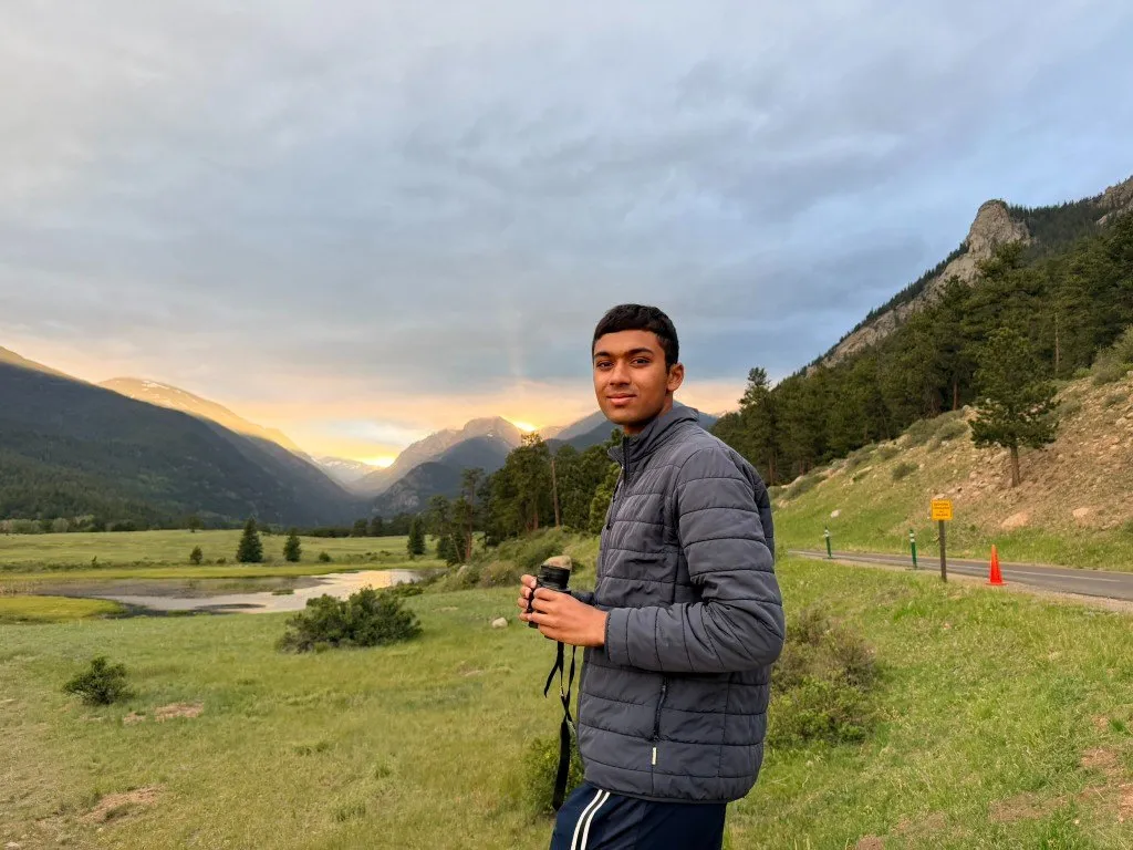 Aditya holding binoculars in a mountain valley at sunset