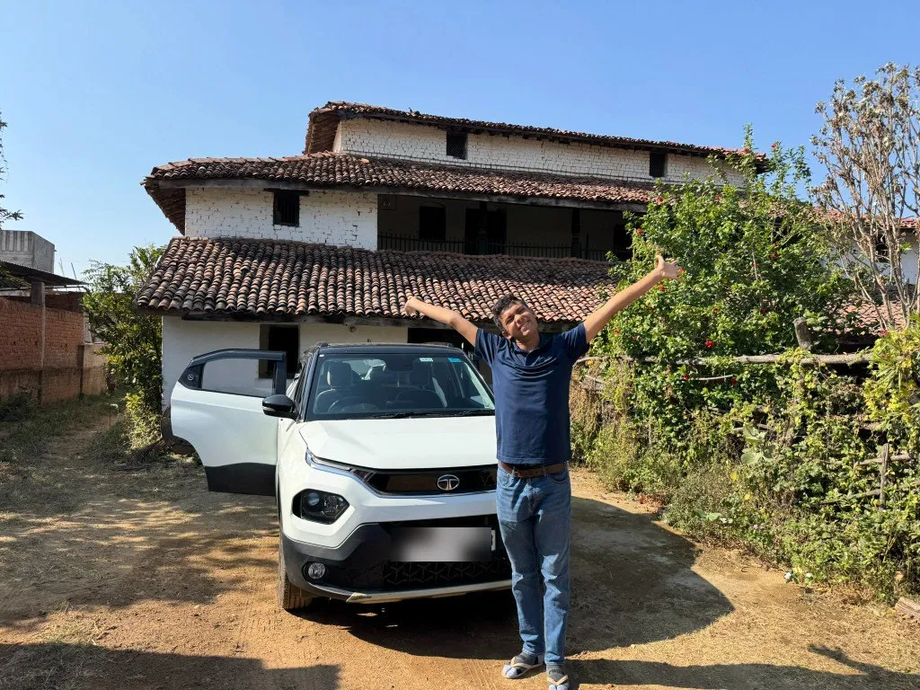 Aditya with his arms spread wide in front of a family home in India