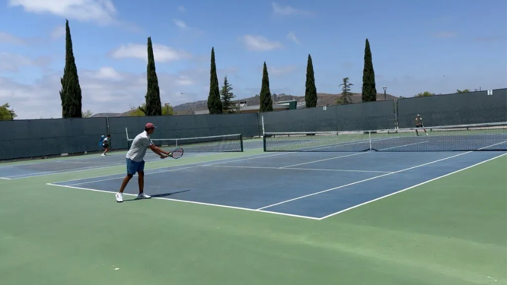 Aditya serving on an outdoor tennis court